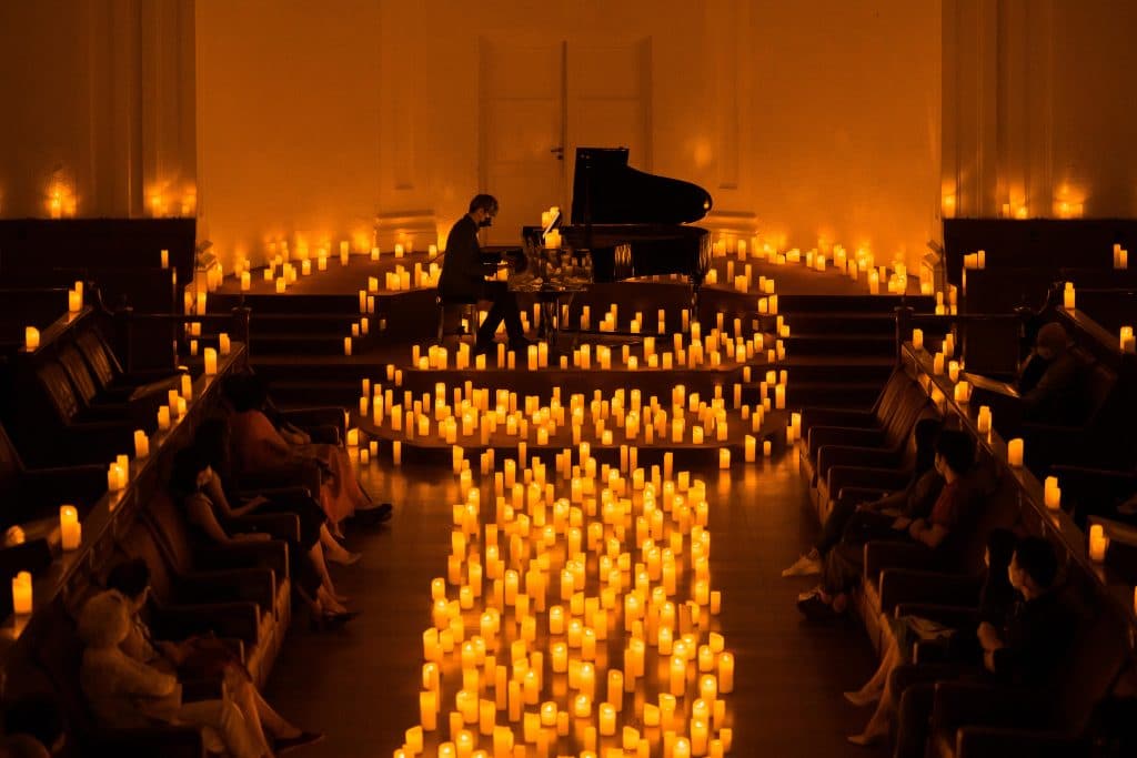 chamber at the arts house lit up with hundreds of candles and a piano in on stage in the distance