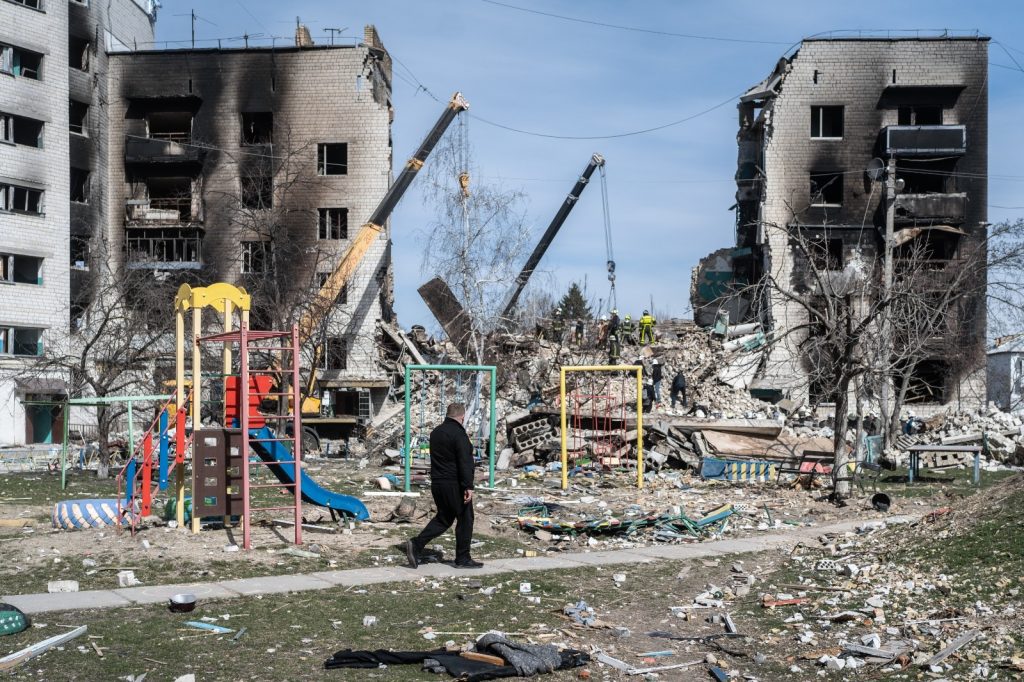 man walking in front of playground in front of destroyed buildings