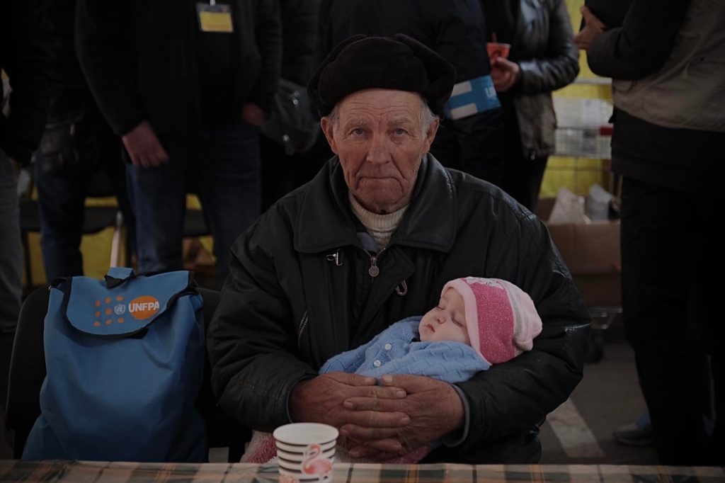 old man craddling baby in refugee shelter