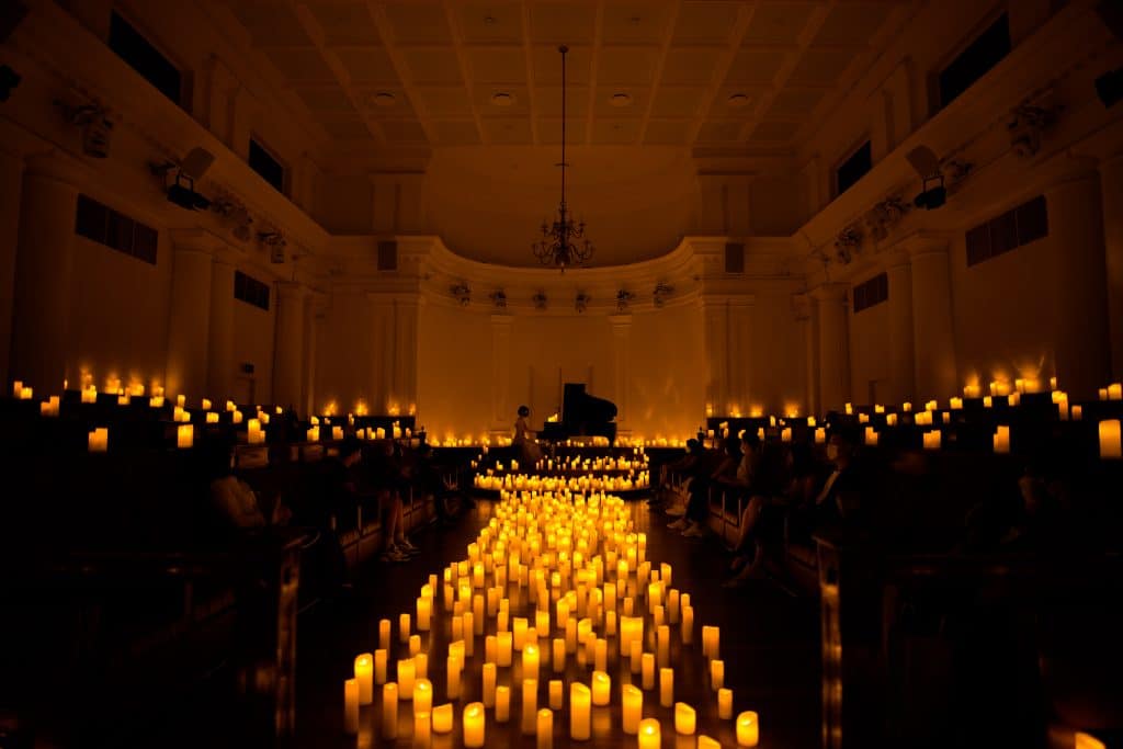 chamber at the arts house lit up with hundreds of candles and a piano in on stage in the distance