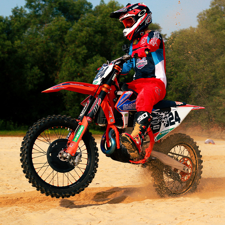 motocross rider on bike along the sand with green forest in the background