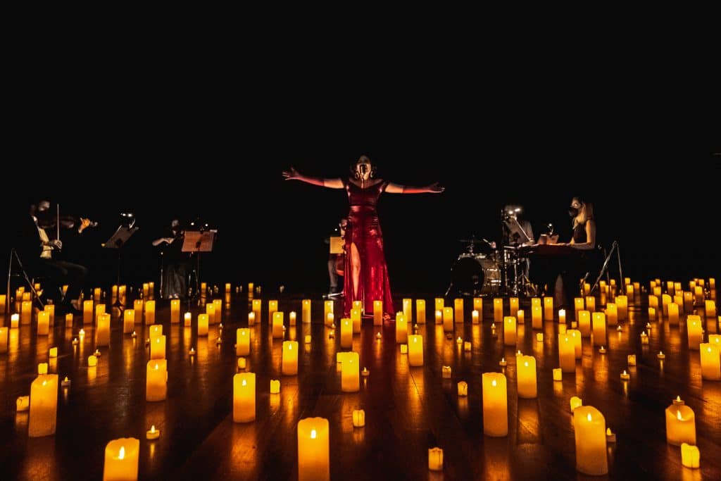 singer in red dress and band surrounded by candles on stage