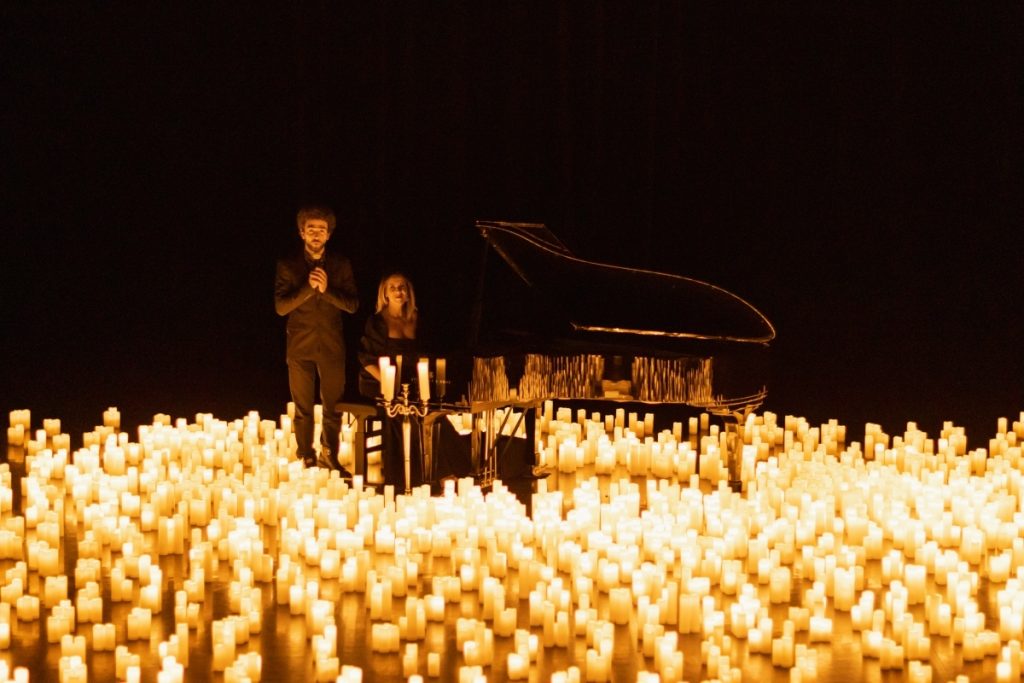 musicians standing beside grand piano surrounded by hundreds of candles