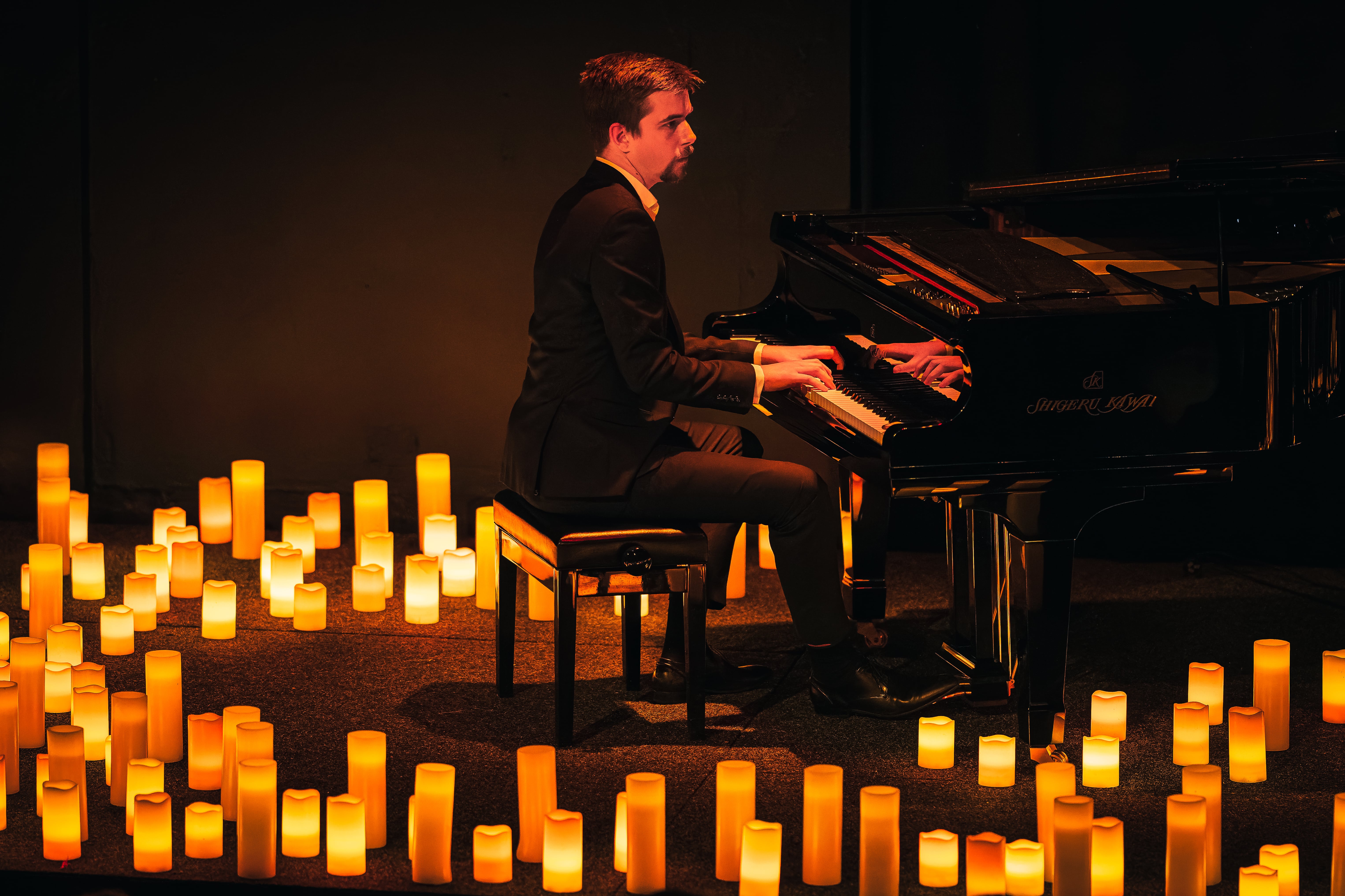 pianist performing surrounded by candles, as seen from the side